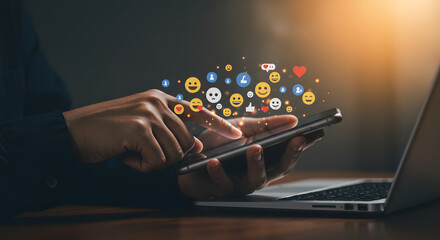 Person using smartphone with social media icons and laptop on the side in dim light setting scene