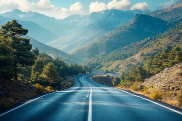 A curving road stretches through a mountainous landscape surrounded by trees and vibrant foliage under a bright sky and distant peaks