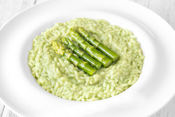 Asparagus risotto served in white plate with whole spears on top