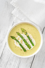 Creamy asparagus soup in white bowl with swirl and toasted ciabatta