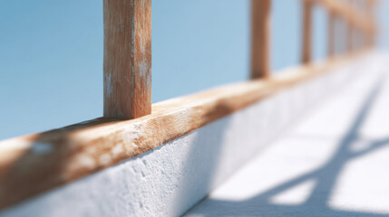 Wooden railing on concrete wall with soft shadows and clear blue sky background in bright daylight