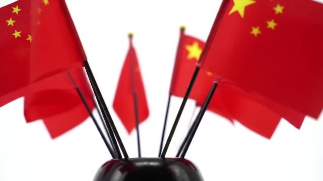 Slow push-in camera toward a group of mini China flags in a stand, pure white background