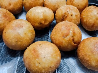 Close-up view of golden-brown deep-fried snack balls, crispy on the outside and likely filled with savory stuffing, arranged neatly on a dark textured surface.