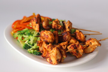Grilled chicken skewers served with stir fried red and yellow capsicum and broccoli on a white plate