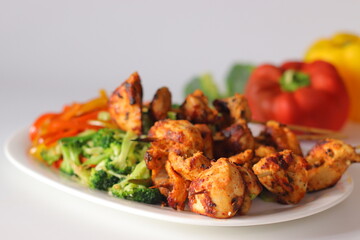Grilled chicken skewers served with stir fried red and yellow capsicum and broccoli on a white plate