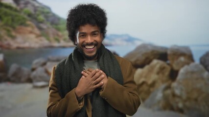 Smiling african american man on seaside beach with rocks in background enjoying peaceful outdoor setting under clear sky with ocean waves and distant mountains