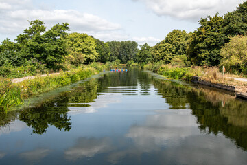 Exeter canal on a beautiful day with strong and vibrant reflections on the water. People can be seen pursuing water sports in the distance. South west England tourism and leisure. Good copy space. 