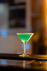 Turquoise cocktail resting on sleek bar counter, warm golden lighting highlighting drink's vivid color and elegant bar atmosphere