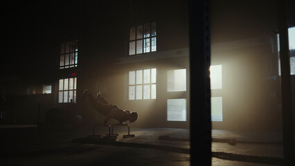 Determined male athlete doing intense dips workout in dramatic gym setting