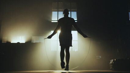 Athlete jumping rope in dark gym with backlight