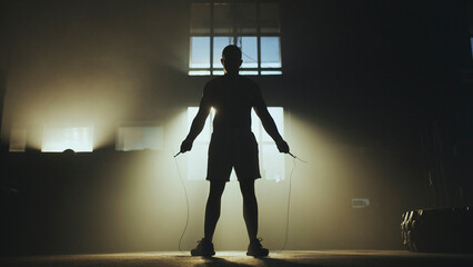 Athlete performing jump rope exercise in dark gym