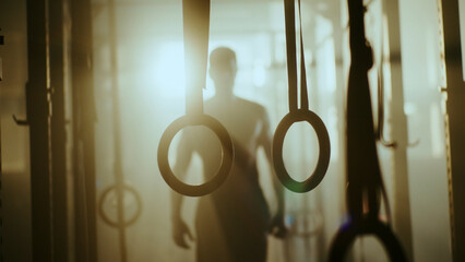 Athlete preparing for gymnastics training with rings in a sunlit gym