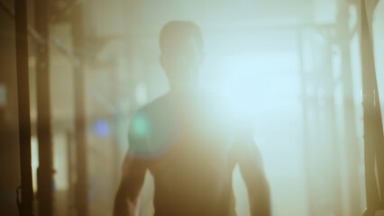 Muscular athlete walking in smoky gym after intense workout