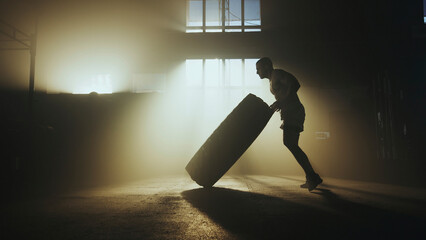 Determined athlete pushing large tire in smoky gym during intense functional training workout