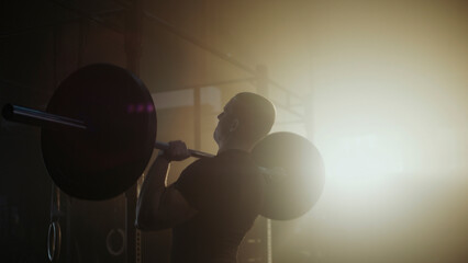 Determined male athlete lifting heavy barbell in smoky gym