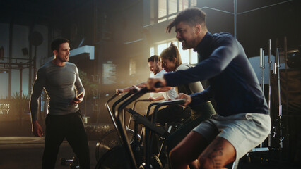 Athletes training with air bikes and personal trainer coaching in gym