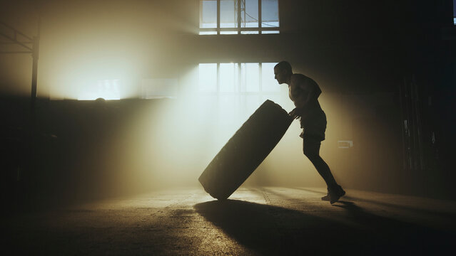 Determined athlete pushing large tire in smoky gym during intense functional training workout - Powered by Adobe