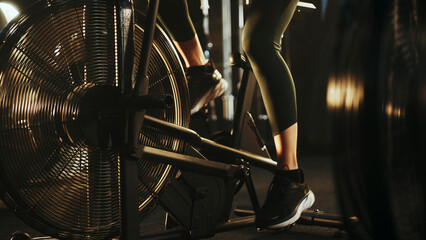Athlete doing air bike exercise in dark gym