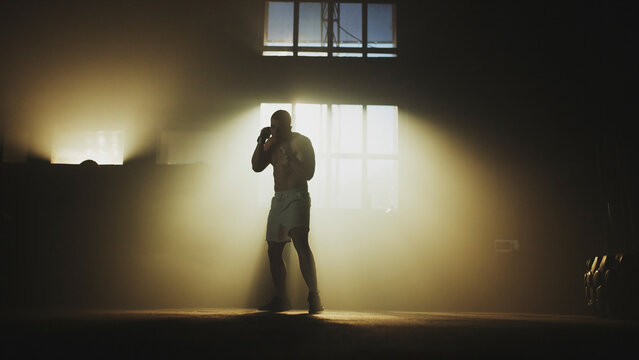 Boxer training in dramatic lighting with atmospheric smoke in gym - Powered by Adobe