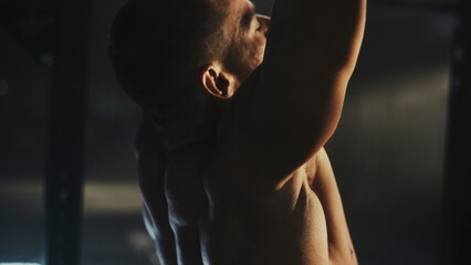 Bodybuilder performing pull-ups showing defined back muscles in dramatic lighting