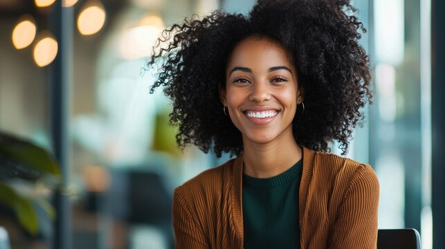 A young woman with curly hair smiling in a modern office setting.