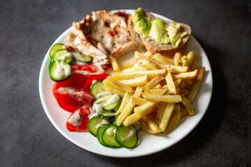 Delicious plate of french fries with fresh salad, avocado bread, and chicken on gray background.