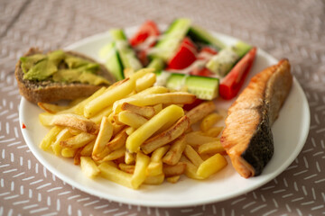 Salmon fillet with fries, avocado toast, and fresh salad on white plate.