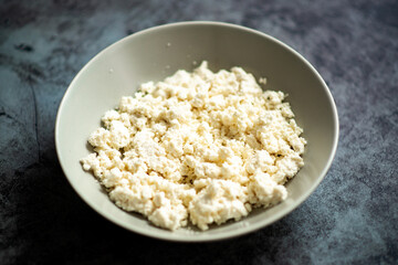 Fresh homemade cottage cheese in a bowl on dark marble background.
