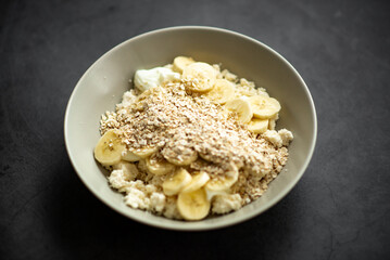 Healthy bowl of oatmeal with bananas and yogurt on dark background.