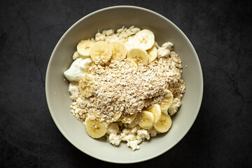 Healthy breakfast bowl with bananas, oats, and yogurt on dark background.
