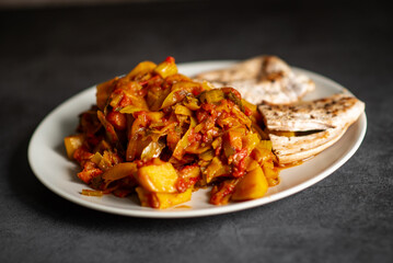 Spicy stir-fried vegetables with grilled flatbread on white plate.