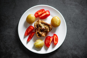Delicious roast chicken with potatoes and tomatoes on white plate.