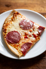 Delicious pepperoni pizza slice on white plate with melty cheese and crispy crust.