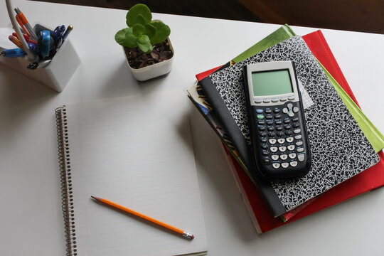 a study station desk with a notebook pencil, graphing calculator, books and essentials with soft lighting. back to school design or banner. - Powered by Adobe