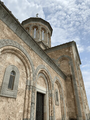 Close-up view of an ornate stone church facade with arched windows and detailed carvings under a partly cloudy sky, example of traditional Eastern Orthodox architecture