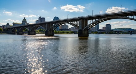 Naklejka premium Arched bridge spans calm water, cityscape in background under a blue sky