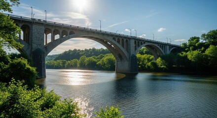 Obraz premium Arched bridge spans a wide river under a bright sun, lined by green trees