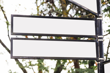 Blank directional sign boards on metal pole. Three empty arrow panels with black frames. Outdoor signage against blurred green foliage background. Space for custom text or symbols.