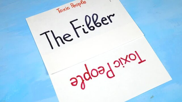 Words 'The Fibber" handwritten on a white sheet of paper. Sheets of paper with written theses on the topic &laquo;Toxic People&raquo; are on a blue background 