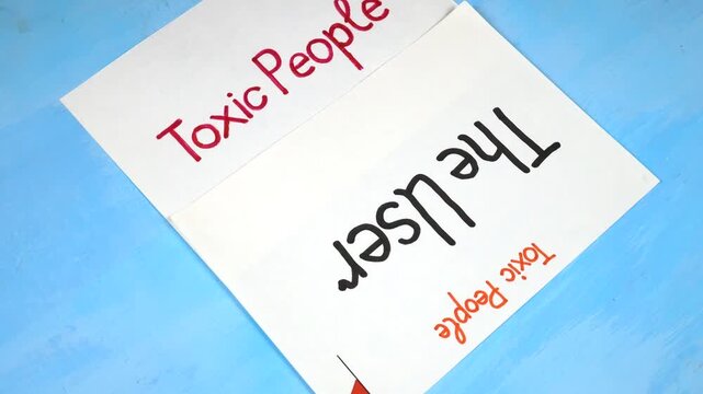 Word &ldquo;The User&rdquo; handwritten on a white sheet of paper. Sheets of paper with written theses on the topic &laquo;Toxic People&raquo; are on a blue background 