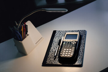 Studying at night. A desk setup with a notebook, calculator, pen, lamp, and holder. Education, college prep, back to school, or university background.
