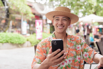 Hispanic man using smartphone texting at outdoor cafe wearing Panama hat and short sleeve shirt
