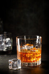 Glass of scotch whiskey with ice cubes on black background
