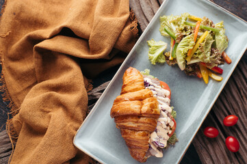 Overhead View of Croissant Sandwich with Side Salad and Cherry Tomatoes on Rustic Wooden Background