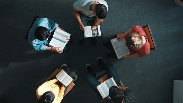 Top down view of prayer reading at bible book and sitting in circle with bible book on laps. Aerial view of diverse people looking at book while studying with faith, trust and hope, calm. Symposium.