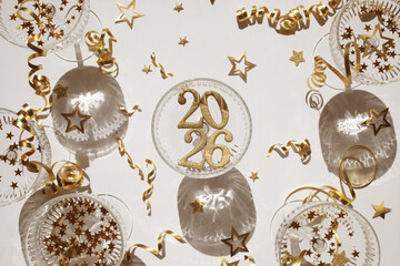 2026 Happy New Year glittering golden numbers in champagne glasses with festive party decoration top view.