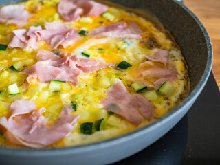 Frittata - scrambled eggs with zucchini and boiled ham in frying pan