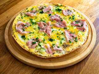 Frittata - scrambled eggs with zucchini and boiled ham on wooden table	