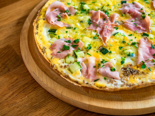Frittata - scrambled eggs with zucchini and boiled ham on wooden table	