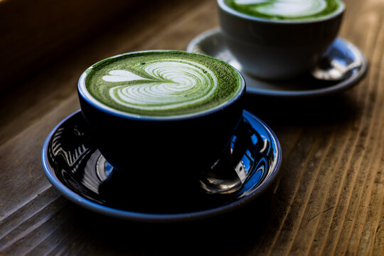Two cups of matcha latte on a dark wooden table